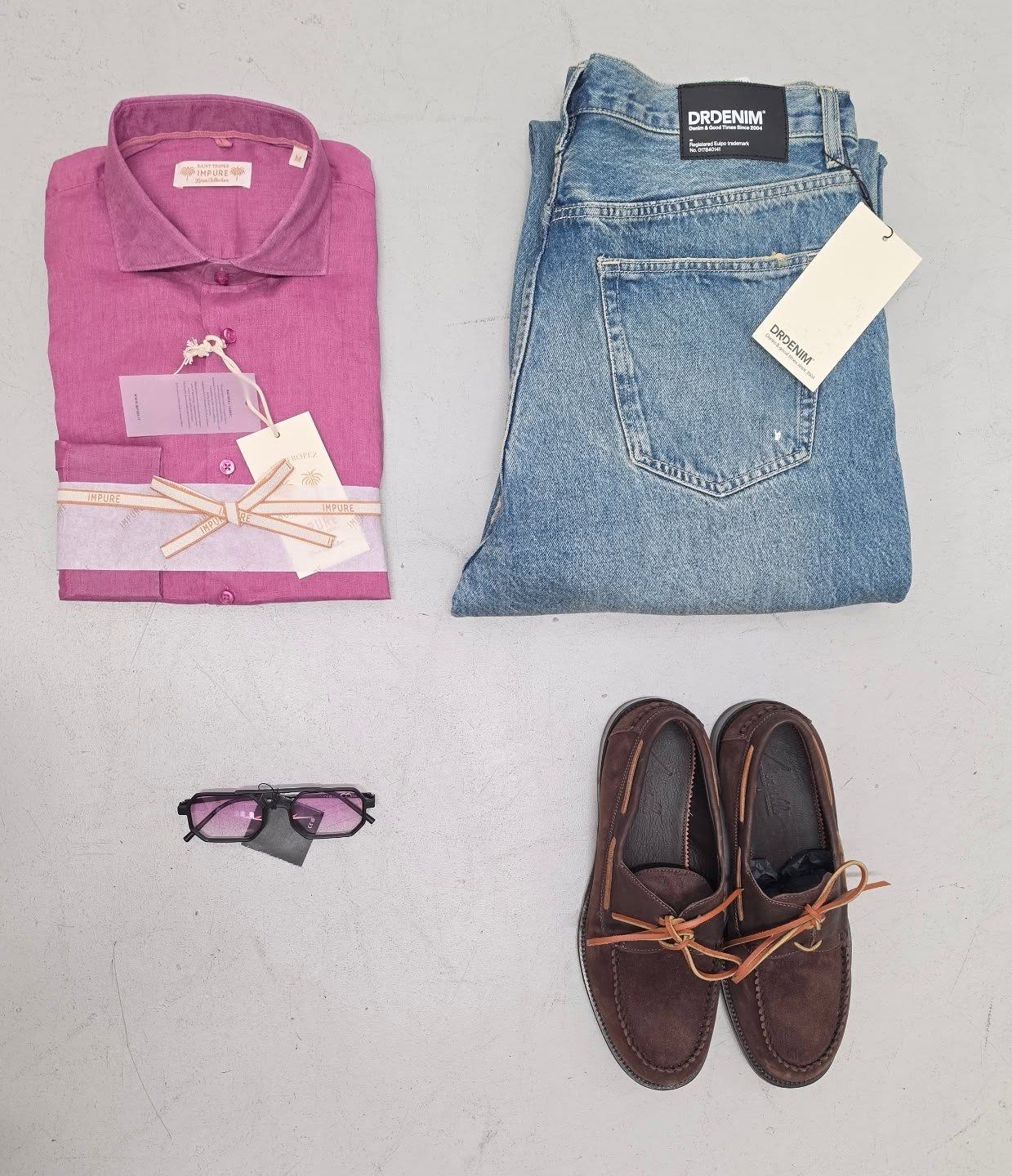 Camicia in lino, jeans, occhiali da sole e mocassini scamosciati disposti insieme in un look uomo